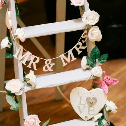 Witte houten ladder met een Mr & Mrs-slinger en rozen.