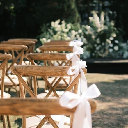 Houten stoelen met witte strikken voor een bloemenboog.