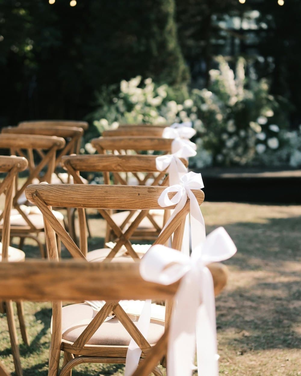 Houten stoelen met witte strikken, klaar voor een ceremonie in de tuin.